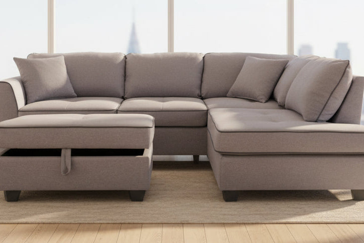 Full view of the Jupiter Grey Fabric Reversible Sectional Sofa, showcasing the neutral upholstery and the matching storage ottoman placed next to the chaise.